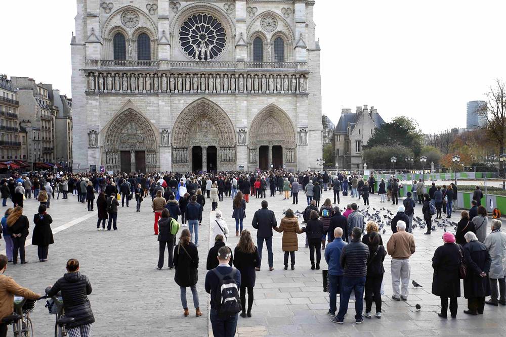 People observe a minute of silence in front of the Notre Dame Cathedral in Paris to pay tribute to victims of Friday's Paris attacks