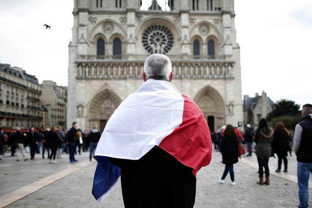 A man, wrapped with a French flag, observes a minute of silence at the Notre Dame Cathedral in Paris to pay tribute to victims of Friday’s Paris attacks