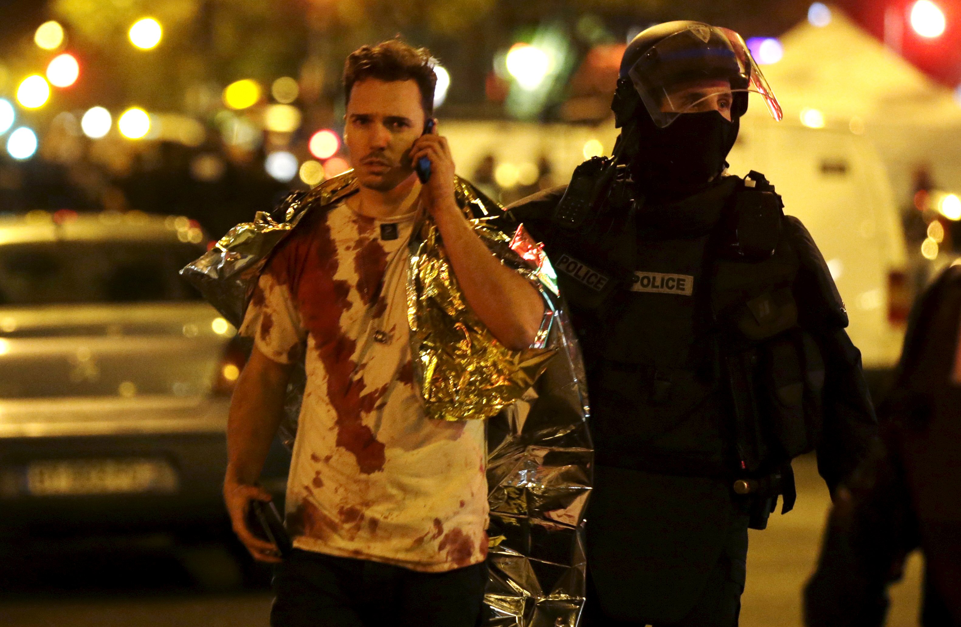 A French policeman assists a blood-covered victim near the Bataclan concert hall following attacks in Paris, France