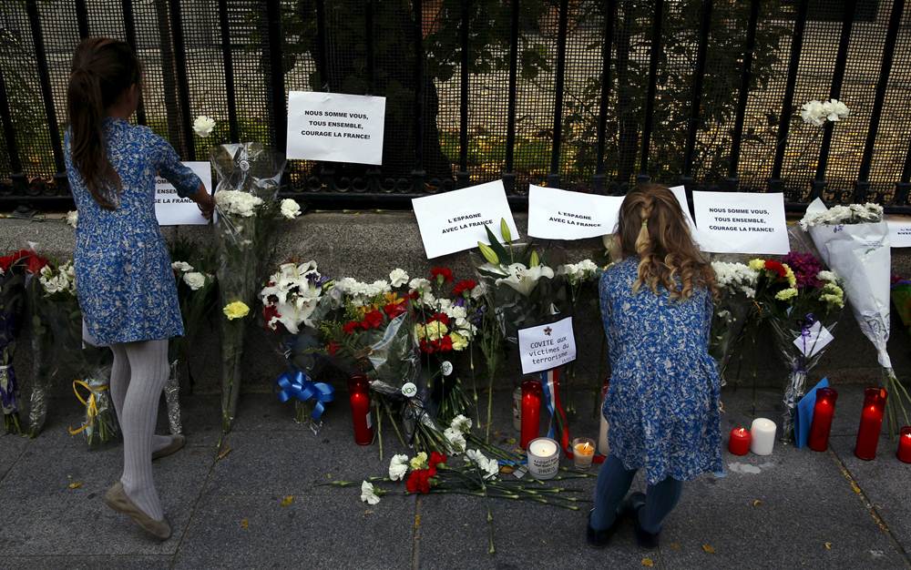 Women place papers next to candles and flowers in memory of victims of deadly attacks in Paris, outside the French embassy in Madrid