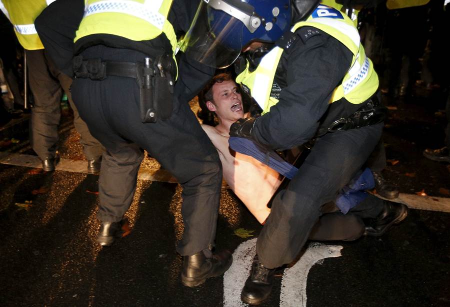 A supporter of the activist group Anonymous is detained by police officers during a protest in London.