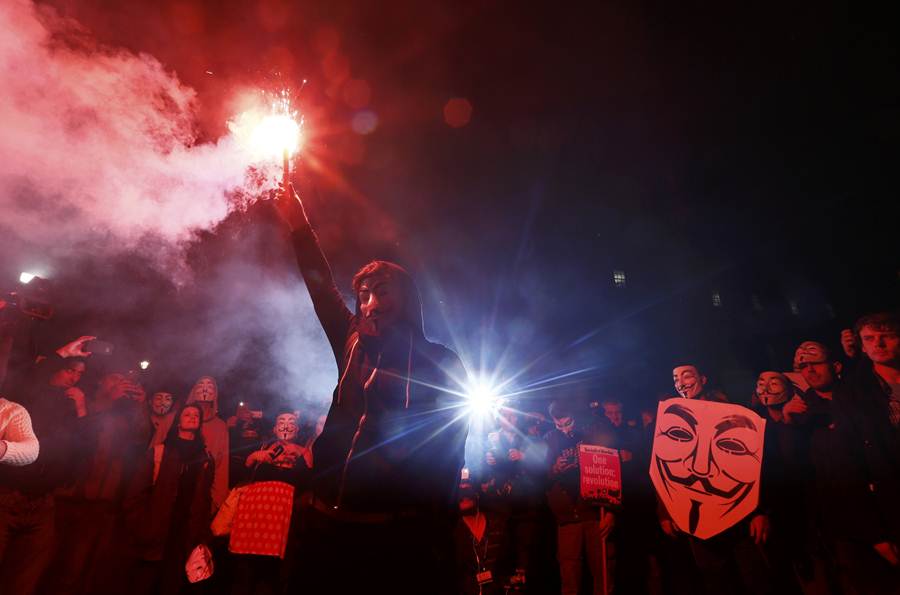 A supporter of the activist group Anonymous holds a flare during a protest in London