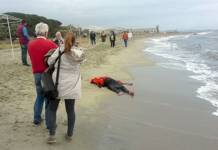 Varias personas observan el cuerpo sin vida de un refugiado en una playa de Ayvalik. | REUTERS